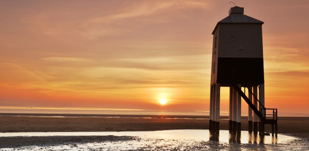 The wooden lighthouse on the beach at sunset.