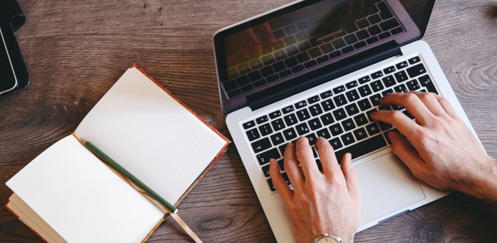 Open notebook on a wooden table, a wristwatch and a pen, analog camera, a laptop. Writer