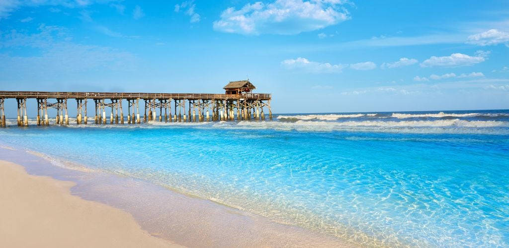 A pier towards to sea, a clear blue sky, and crystal clear water.