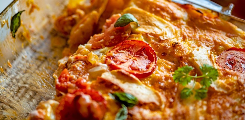 In a casserole dish, serve vegetable lasagna with a tomato and green leaf garnish on top.