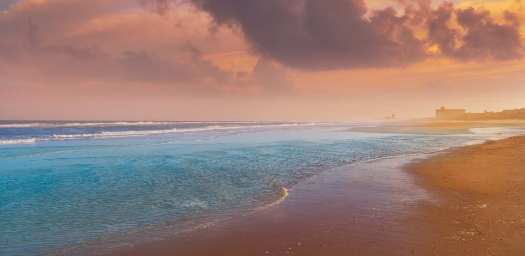 A beach with clear blue sea at sunset.