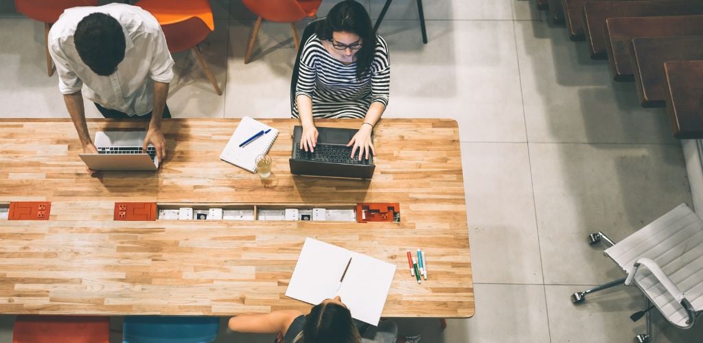 Overhead view on three business people working on desk in office.