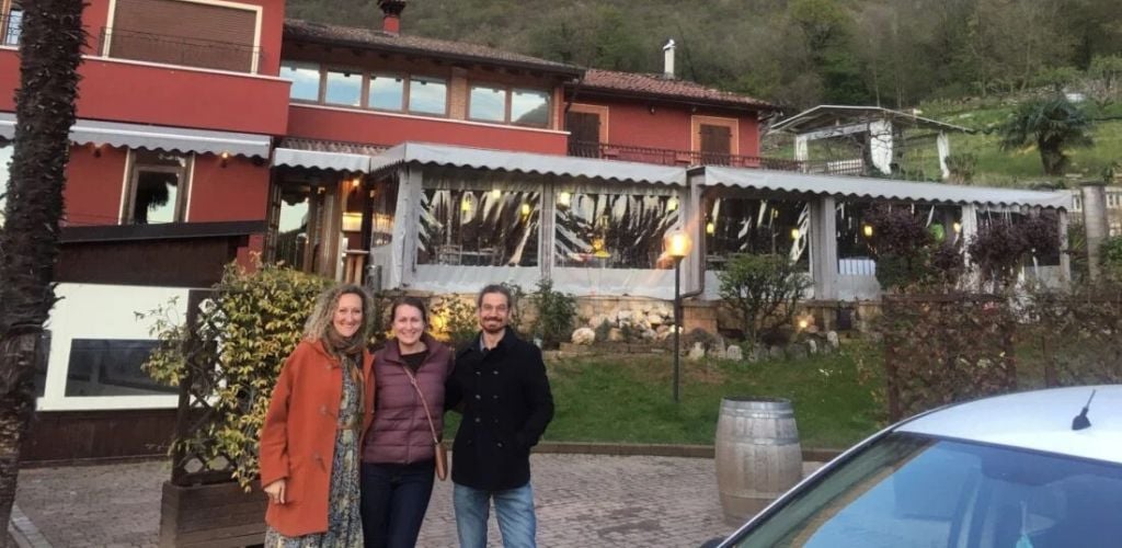 Two women and a man standing in front of a vacation house and a car in the side.